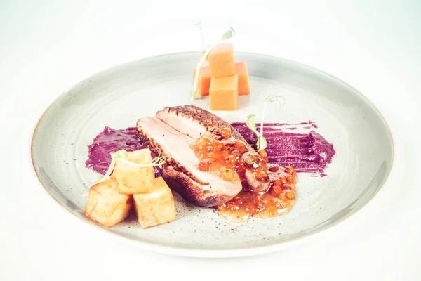 Roast duck breast, red cabbage with apple, roasted potatoes,mountain ash and honey sauce on a plate on a white backgorund