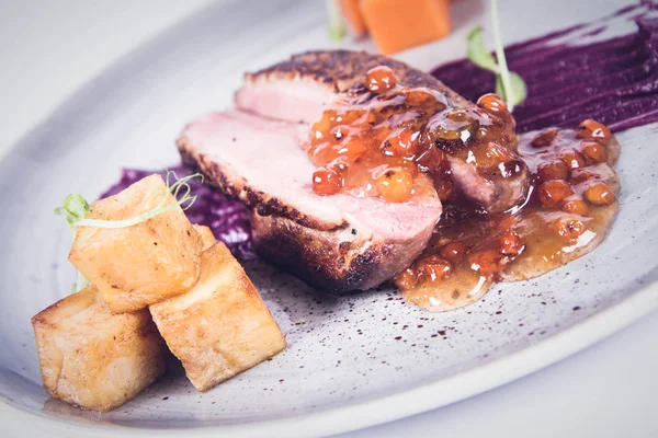 Roast duck breast, red cabbage with apple, roasted potatoes,mountain ash and honey sauce on a plate on a white backgorund