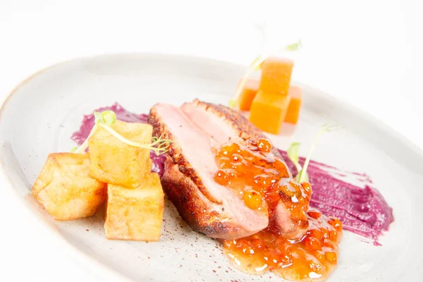 Roast duck breast, red cabbage with apple, roasted potatoes,mountain ash and honey sauce on a plate on a white backgorund