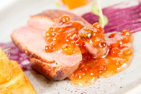 Roast duck breast, red cabbage with apple, roasted potatoes,mountain ash and honey sauce on a plate on a white backgorund