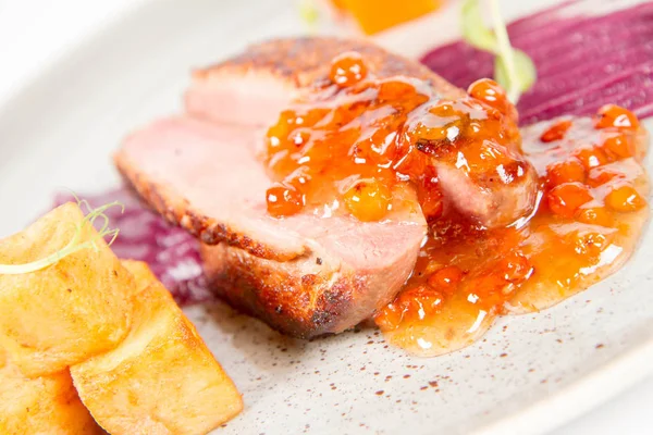 Roast duck breast, red cabbage with apple, roasted potatoes,mountain ash and honey sauce on a plate on a white backgorund