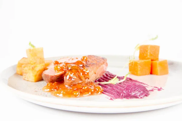 Roast duck breast, red cabbage with apple, roasted potatoes,mountain ash and honey sauce on a plate on a white backgorund