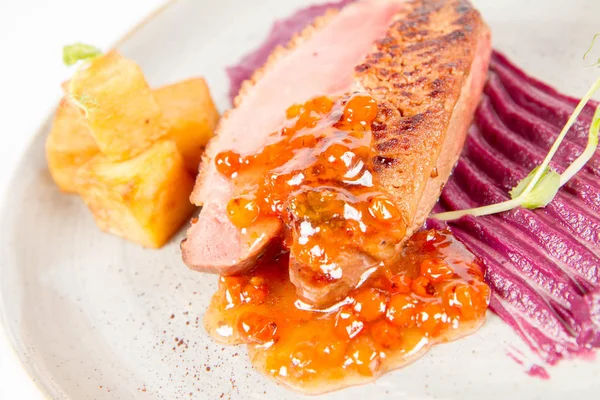 Roast duck breast, red cabbage with apple, roasted potatoes,mountain ash and honey sauce on a plate on a white backgorund