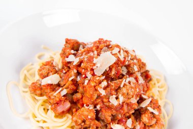 Beyaz arka planda parmesanlı spagetti bolonez serpilmiş.