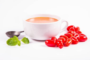 Taze naneyle süslenmiş gazpacho çorbası ve beyaz arka planda eski kaşık ile süslenmiş domates.