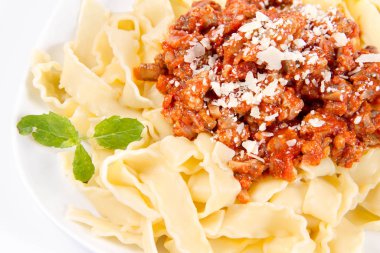 Parmesanla süslenmiş bolonez soslu reginette makarna ve beyaz arka planda taze otlar.