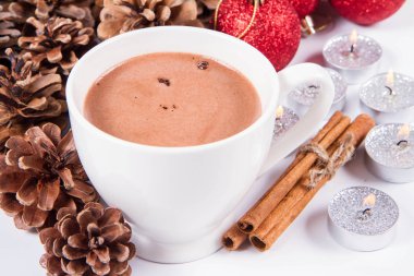 Bir fincan sıcak çikolata, tarçın çubukları, koniler, noel baloları ve mumlar.