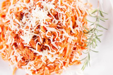 Biberiye dalıyla süslenmiş ve üzerine peynir serpiştirilmiş bir tabak spagetti bolonez.