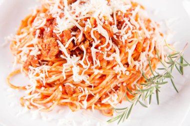 Biberiye dalıyla süslenmiş ve üzerine peynir serpiştirilmiş bir tabak spagetti bolonez.