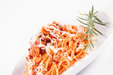 Biberiye dalıyla süslenmiş ve üzerine peynir serpiştirilmiş bir tabak spagetti bolonez.