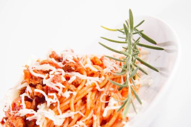 Biberiye dalıyla süslenmiş ve üzerine peynir serpiştirilmiş bir tabak spagetti bolonez.