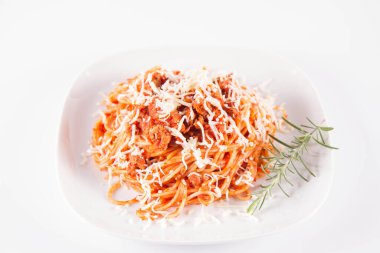Biberiye dalıyla süslenmiş ve üzerine peynir serpiştirilmiş bir tabak spagetti bolonez.