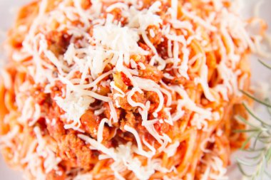 Biberiye dalıyla süslenmiş ve üzerine peynir serpiştirilmiş bir tabak spagetti bolonez.
