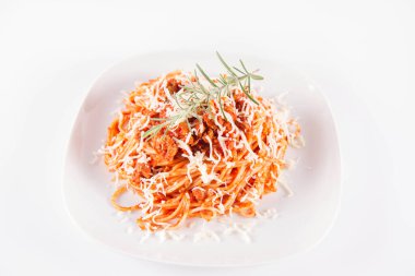 Biberiye dalıyla süslenmiş ve üzerine peynir serpiştirilmiş bir tabak spagetti bolonez.