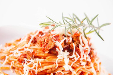 Biberiye dalıyla süslenmiş ve üzerine peynir serpiştirilmiş bir tabak spagetti bolonez.