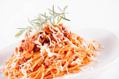 Biberiye dalıyla süslenmiş ve üzerine peynir serpiştirilmiş bir tabak spagetti bolonez.