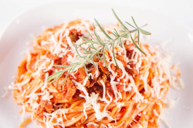Biberiye dalıyla süslenmiş ve üzerine peynir serpiştirilmiş bir tabak spagetti bolonez.