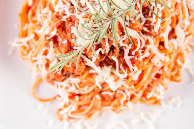Biberiye dalıyla süslenmiş ve üzerine peynir serpiştirilmiş bir tabak spagetti bolonez.
