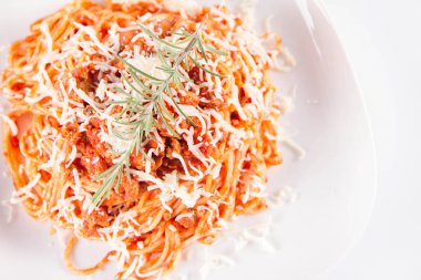 Biberiye dalıyla süslenmiş ve üzerine peynir serpiştirilmiş bir tabak spagetti bolonez.