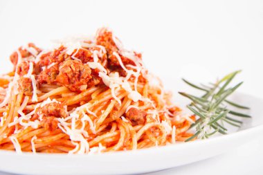 Biberiye dalıyla süslenmiş ve üzerine peynir serpiştirilmiş bir tabak spagetti bolonez.
