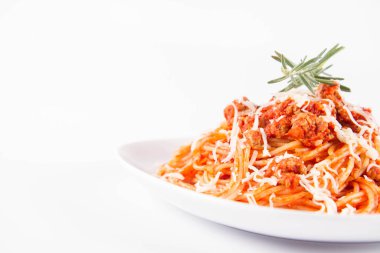 Biberiye dalıyla süslenmiş ve üzerine peynir serpiştirilmiş bir tabak spagetti bolonez.