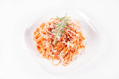 Biberiye dalıyla süslenmiş ve üzerine peynir serpiştirilmiş bir tabak spagetti bolonez.