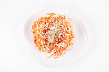 Biberiye dalıyla süslenmiş ve üzerine peynir serpiştirilmiş bir tabak spagetti bolonez.