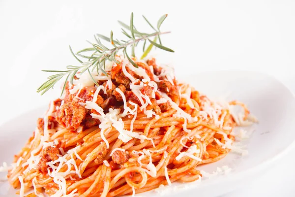 Biberiye dalıyla süslenmiş ve üzerine peynir serpiştirilmiş bir tabak spagetti bolonez.