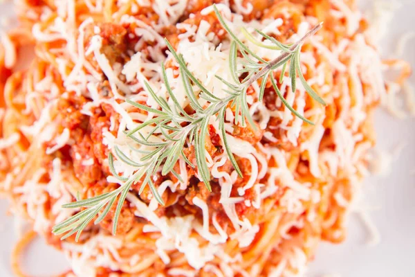 Biberiye dalıyla süslenmiş ve üzerine peynir serpiştirilmiş bir tabak spagetti bolonez.