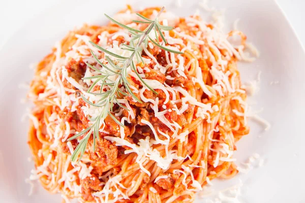 Biberiye dalıyla süslenmiş ve üzerine peynir serpiştirilmiş bir tabak spagetti bolonez.