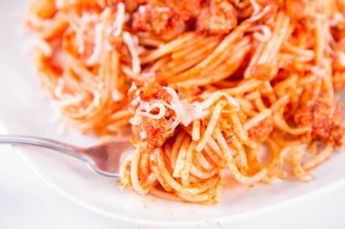 Çatalla yenmiş peynirle kaplı bir tabakta spagetti bolonez.