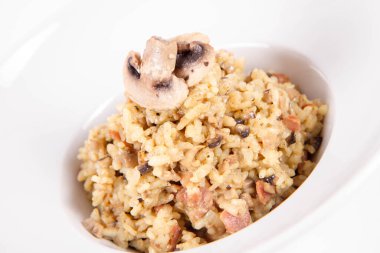 Mantarlı risotto ve beyaz arka planda mantarla süslenmiş domuz pastırması.