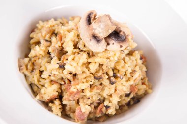 Mantarlı risotto ve beyaz arka planda mantarla süslenmiş domuz pastırması.