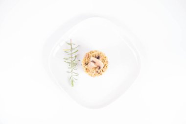 Mantarlı risotto ve mantarlı pastırma ve beyaz arka planda bir tabakta biberiye dalı ile süslenmiş.