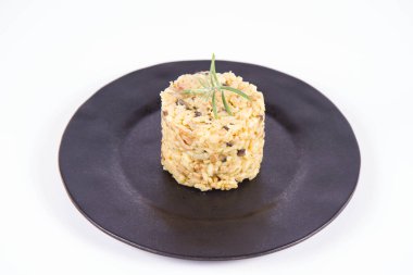 Düğme mantarlı risotto ve beyaz arka planda siyah bir tabakta biberiye dalı ile süslenmiş domuz pastırması.