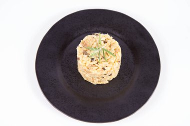 Düğme mantarlı risotto ve beyaz arka planda siyah bir tabakta biberiye dalı ile süslenmiş domuz pastırması.