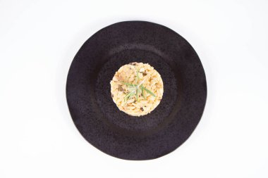 Risotto with button mushroom and bacon decorated with rosemary twig on a black plate on a white background clipart