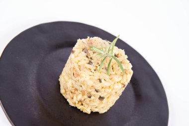 Düğme mantarlı risotto ve beyaz arka planda siyah bir tabakta biberiye dalı ile süslenmiş domuz pastırması.