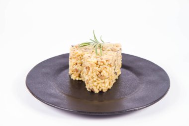 Kalp şeklinde Risotto porsiyonu, düğme mantarlı ve pastırmalı. Beyaz arka planda siyah bir tabakta biberiye dalıyla süslenmiş.