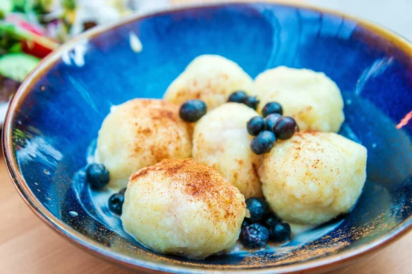 Six homemade sweet dumplings served with vanilla cream and blueberries in blue ceramic vintage bowl