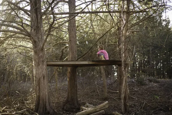 Ağaçlar arasında ahşap yüzey üzerinde oturan kız — Stok fotoğraf
