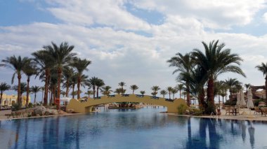 Mısır beldesinde. Avuç içi ve bir köprü mavi gökyüzü beyaz bulutlar ile karşı havuz suyu yansıtılır