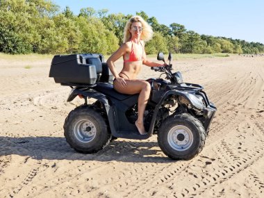 uzun sarı saçlı bikini çekici kadın dört bisiklet, güneşli bir gün oturuyor.