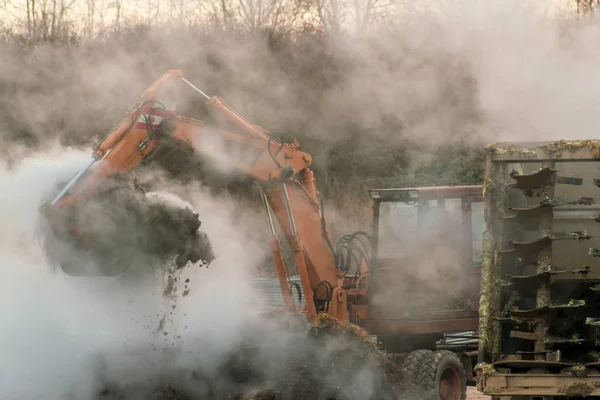 Excavator loads manure, hovering in the cold air, into a tractor with a trailer Stock Photo