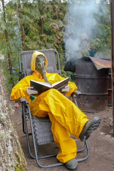 一个戴着防毒面具 身穿黄色防护服的人坐在那里看书 免版税图库图片
