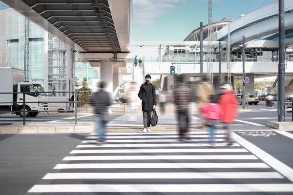 Genç adam siyah maske takıyor ve elektrikli tren istasyonunun yakınındaki beton köprünün altından geçmeyi bekliyor.
