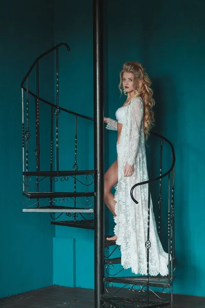 Hermosa novia rubia en negligee blanco caminando por la escalera de hierro forjado negro — Foto de Stock