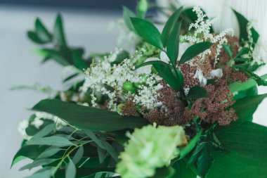 Büyük tropikal yeşil yaprakları ve beyaz çiçeklerle düğün gelin buketi