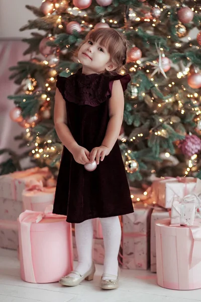 Menina sorridente feliz com brinquedo de Natal perto de uma árvore de xmas — Fotografia de Stock