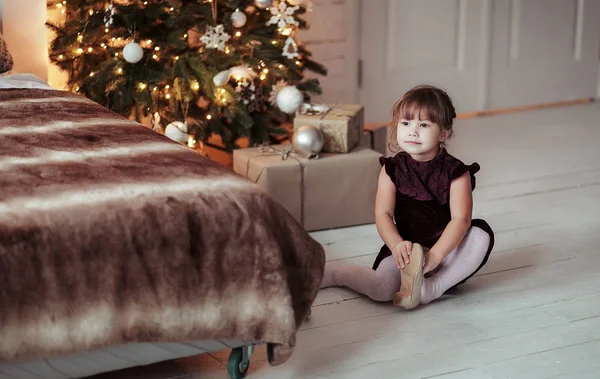 Menina sorridente feliz sentada no chão perto de uma árvore de Natal — Fotografia de Stock